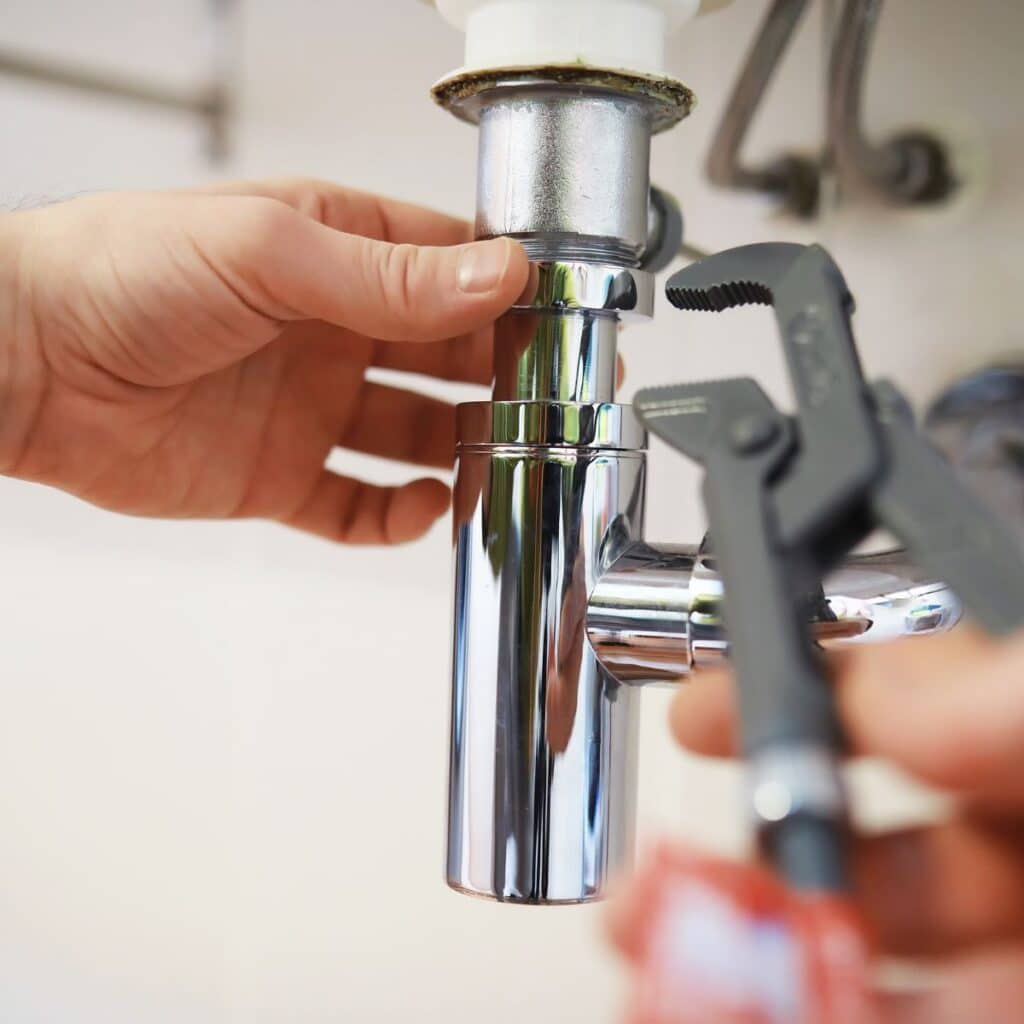 plumber using a pipe wrench to tighten a pipe under a sink