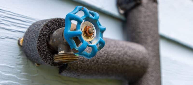 closeup of an outdoor water faucet with insulation installed on the pipes