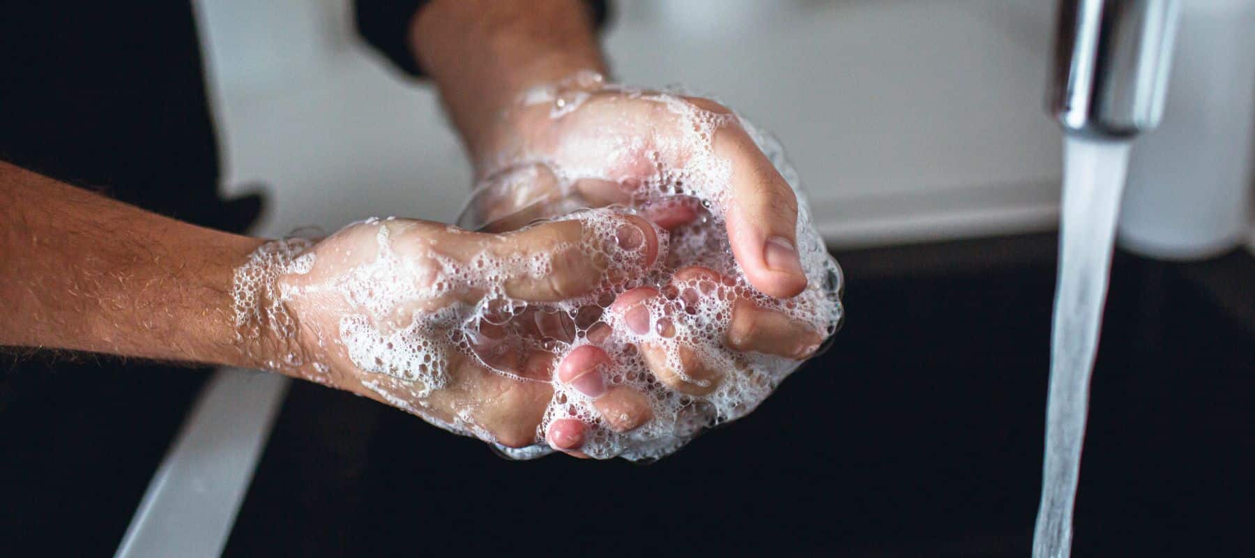 Person washing hands with soap under running water at a sink