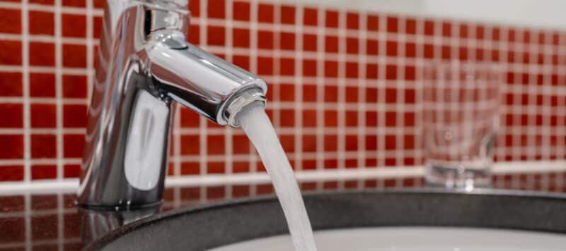 Water flowing from a modern chrome faucet into a sink with red tiled backsplash